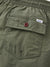 Close-up of the Katin Poolside Volley shorts’ olive green nylon pocket, featuring a red button, small white Katin label above the flap, and elastic waistband—signature details from Katins collection.