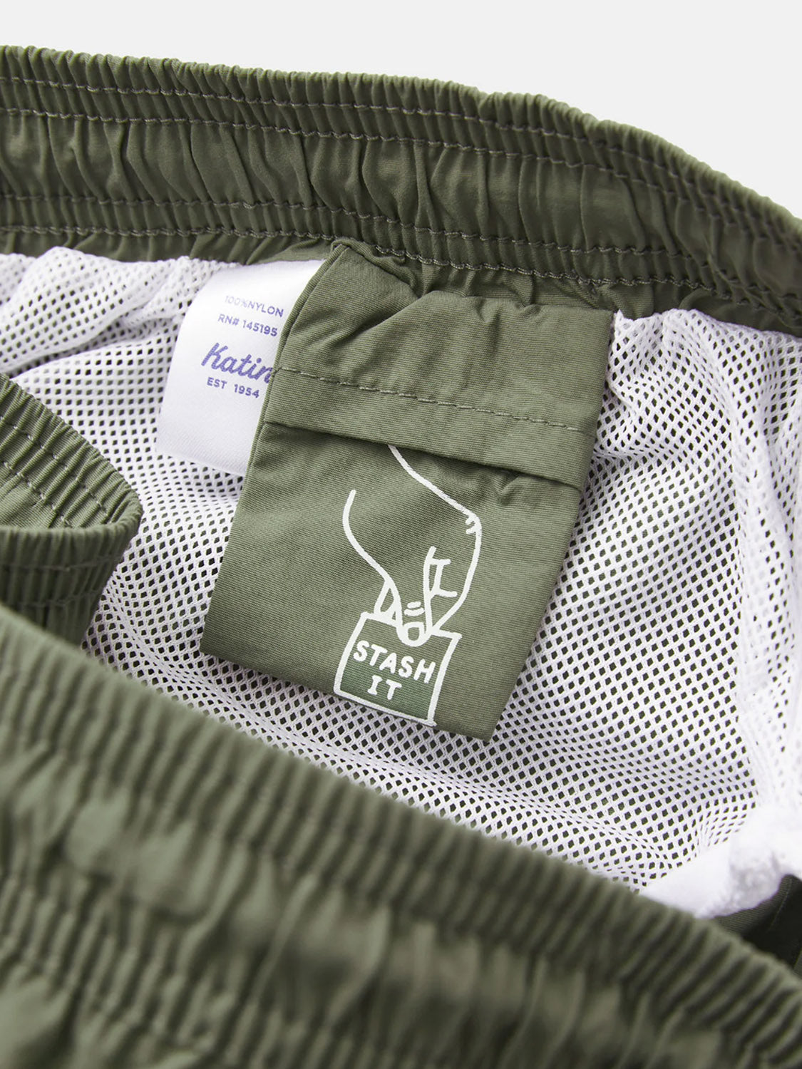 Close-up of the Katin Poolside Volley shorts in green nylon, featuring a mesh brief lining, elastic waistband, an inside STASH IT line-drawing tag, and another tag with Katin branding and fabric details.