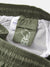 Close-up of the Katin Poolside Volley shorts in green nylon, featuring a mesh brief lining, elastic waistband, an inside STASH IT line-drawing tag, and another tag with Katin branding and fabric details.