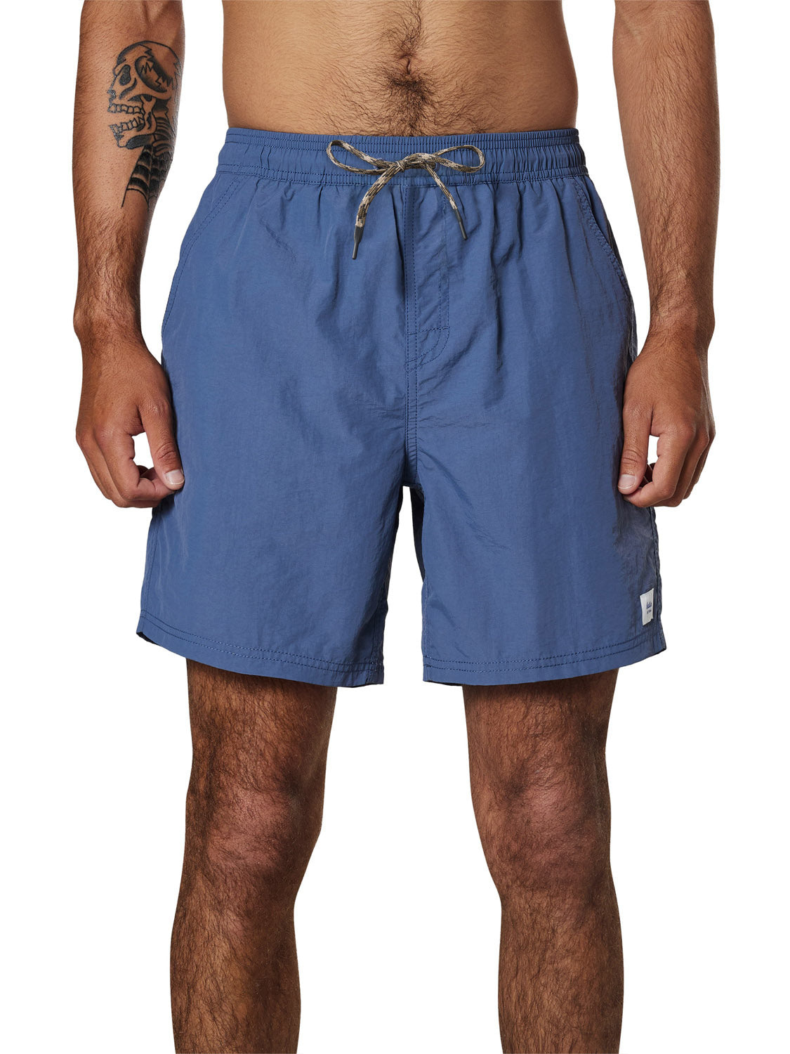 A man with a tattoo on his left arm wears Katin Poolside Volley swim trunks, featuring an elastic waistband, against a white background. Only his torso and legs are shown.