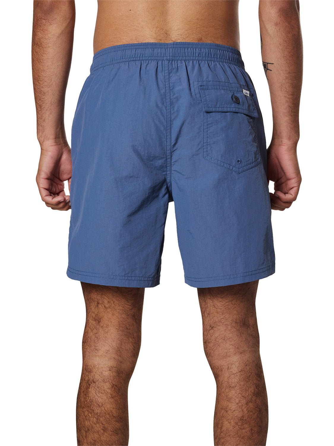 A person faces away from the camera, showing only their lower back and legs in Katin Poolside Volley blue swim trunks by Katin, featuring an elastic waistband and mesh brief lining.