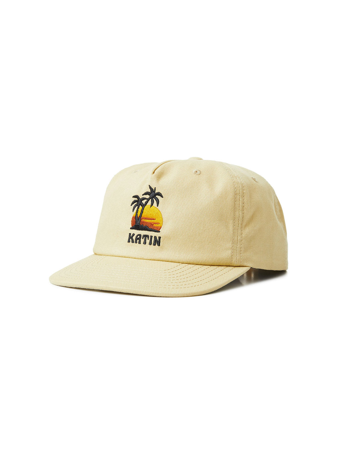 The Katin Voyage Hat is a beige baseball cap featuring custom embroidery of a sunset and palm tree design with KATIN below. Made from cotton twill, it has a flat brim and classic button on top. Part of the Katin headwear collection.