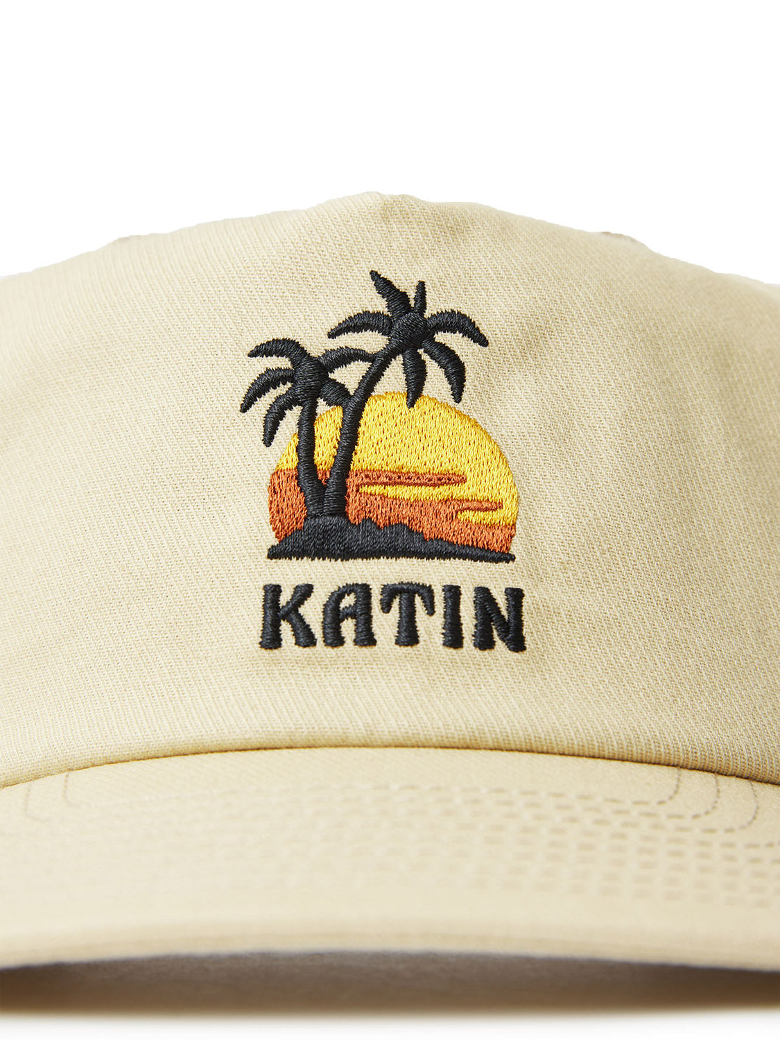 The Katin Voyage Hat is a beige cotton twill cap featuring a custom embroidery design of two palm trees in front of a setting sun, with KATIN stitched below, showcasing Katins commitment to quality and style.