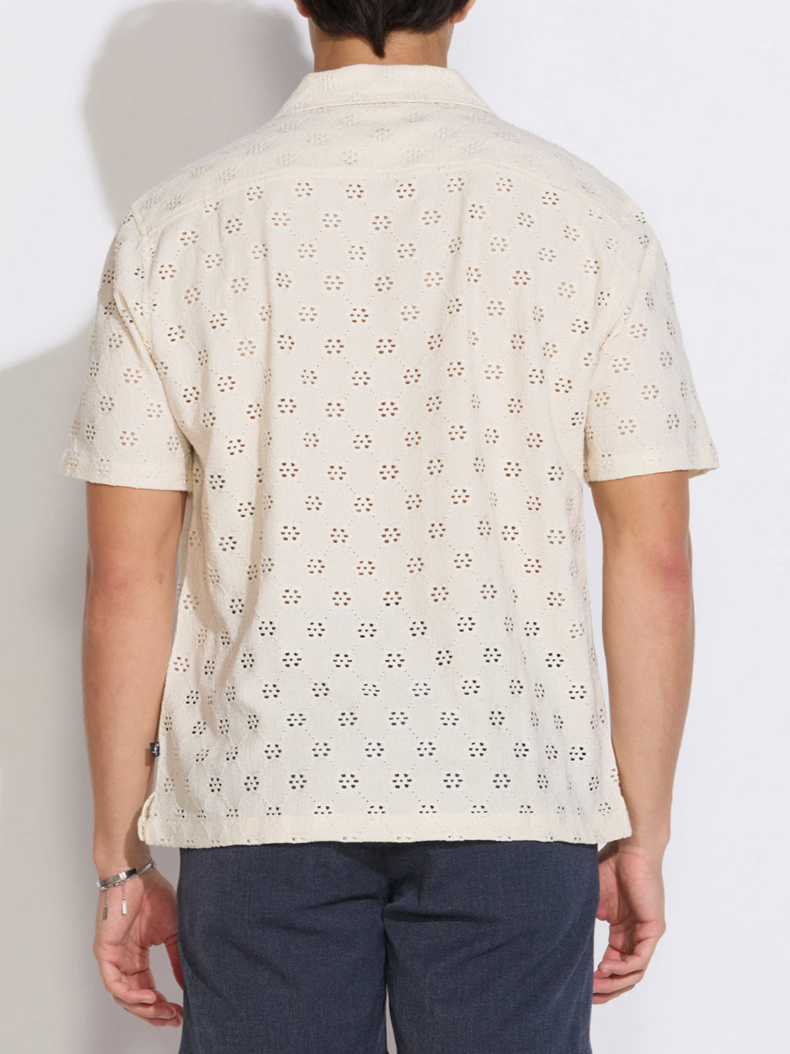 A person wearing the Civil Society Wake Eyelet Knit Resort Shirt in cream with short sleeves and dark pants is shown from the back against a plain white background.