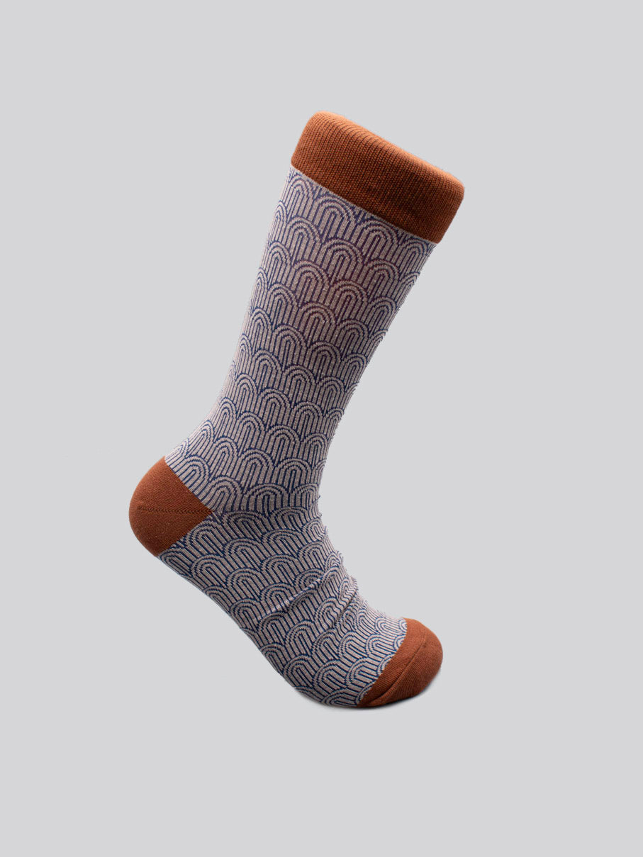 The Waterfall Graphic Sock by ID Menswear fits men’s shoe size 8–12. It features a blue and white scallop pattern with rust accents on the toe, heel, and cuff, crafted from premium combed cotton and shown on a plain light gray background.