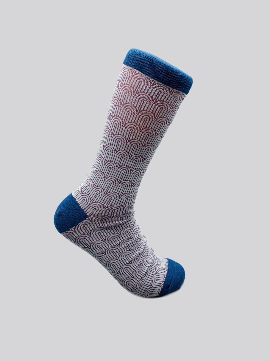 The ID Menswear Waterfall Graphic Socks feature a red and white scallop pattern on a light base with blue toe, heel, and cuff. Made from premium combed cotton, this single sock fits men’s shoe size 8-12 and is shown on a gray surface.