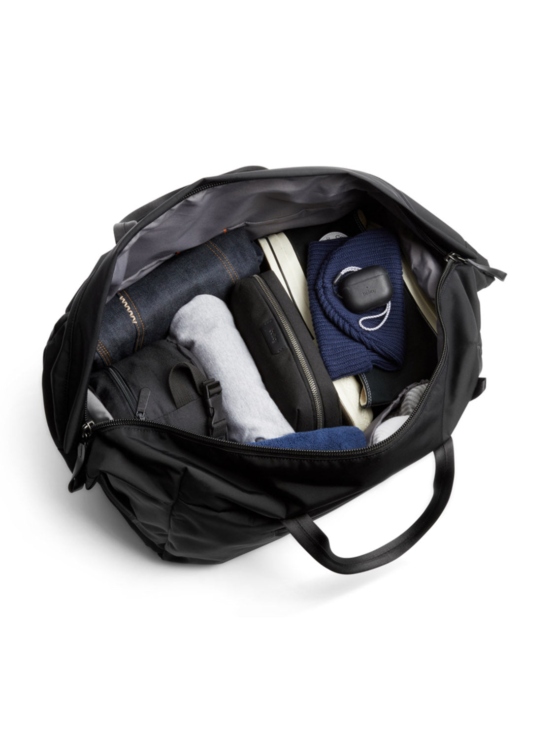 The Bellroy Classic Weekender - 45L, shown open from above on a white background, features handles and spacious storage for clothes, shoes, toiletries, headphones, and a navy sweater—ideal as a minimalist travel bag for weekends.