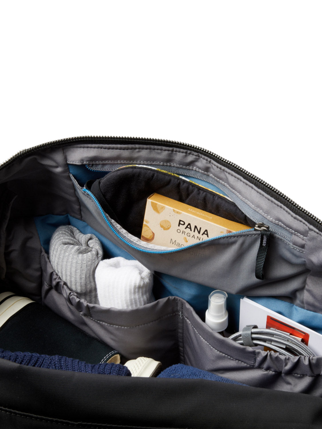 A close-up of the Bellroy Classic Weekender - 45L shows neatly organized socks, a chocolate bar, spray bottle, book, and white sneakers inside. Multiple compartments and a zippered pocket provide easy access to your essentials.