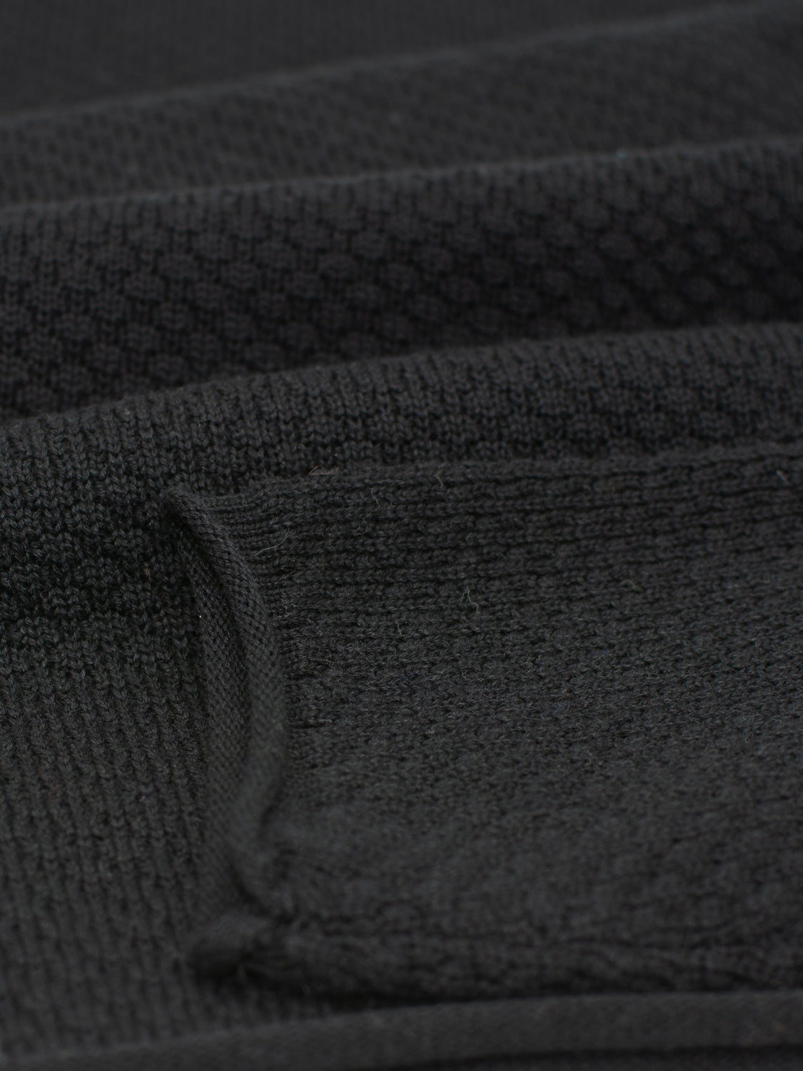 Close-up of the textured, dark fabric with a pocket. The intricate patterns of the Westside Rolled Crew Neck Sweater by ID Menswear showcase detailed artistry, creating a layered look.