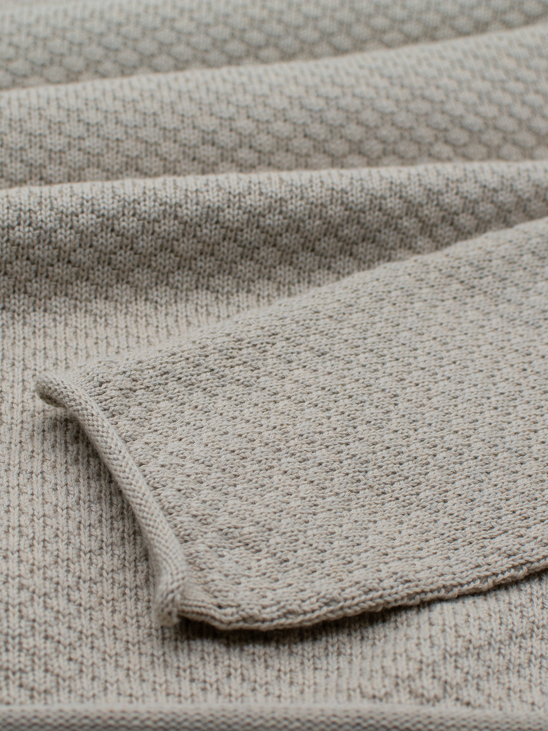 Close-up of a textured beige waffle-knit pattern, similar to ID Menswears Westside Rolled Crew Neck Sweater, with multiple folds showcasing its soft and thick texture. The dense knit adds a cozy, layered look ideal for any knitwear collection.