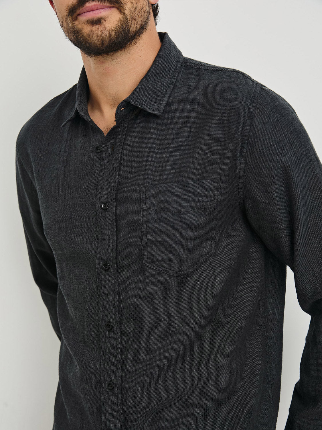 A person wearing the Rails Wyatt Shirt, a dark, classic cotton button-down with a chest pocket, stands against a plain white background. The focus is on their upper body, with their face partially out of view.