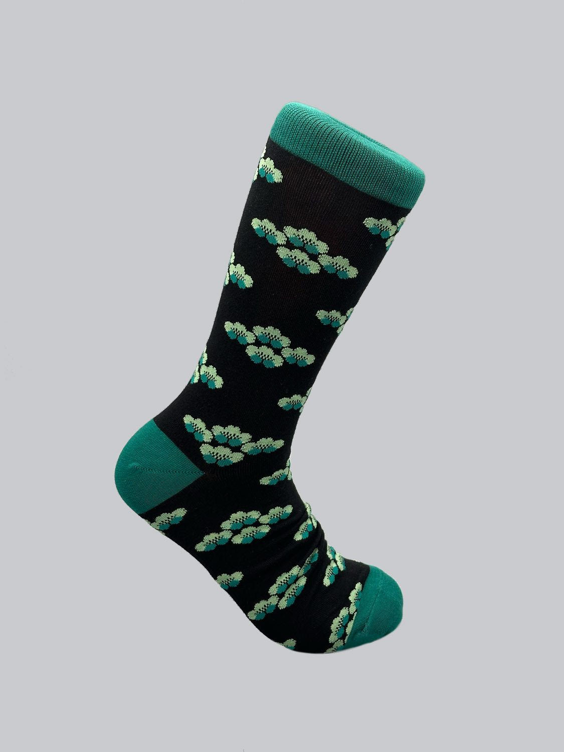 The Yuki Graphic Socks by ID Menswear feature a single black sock with green accents and a light gray background, showcasing a pattern of light green, teal, and yellow flowers. Made from luxurious combed cotton, the heel, toe, and cuff are solid green.