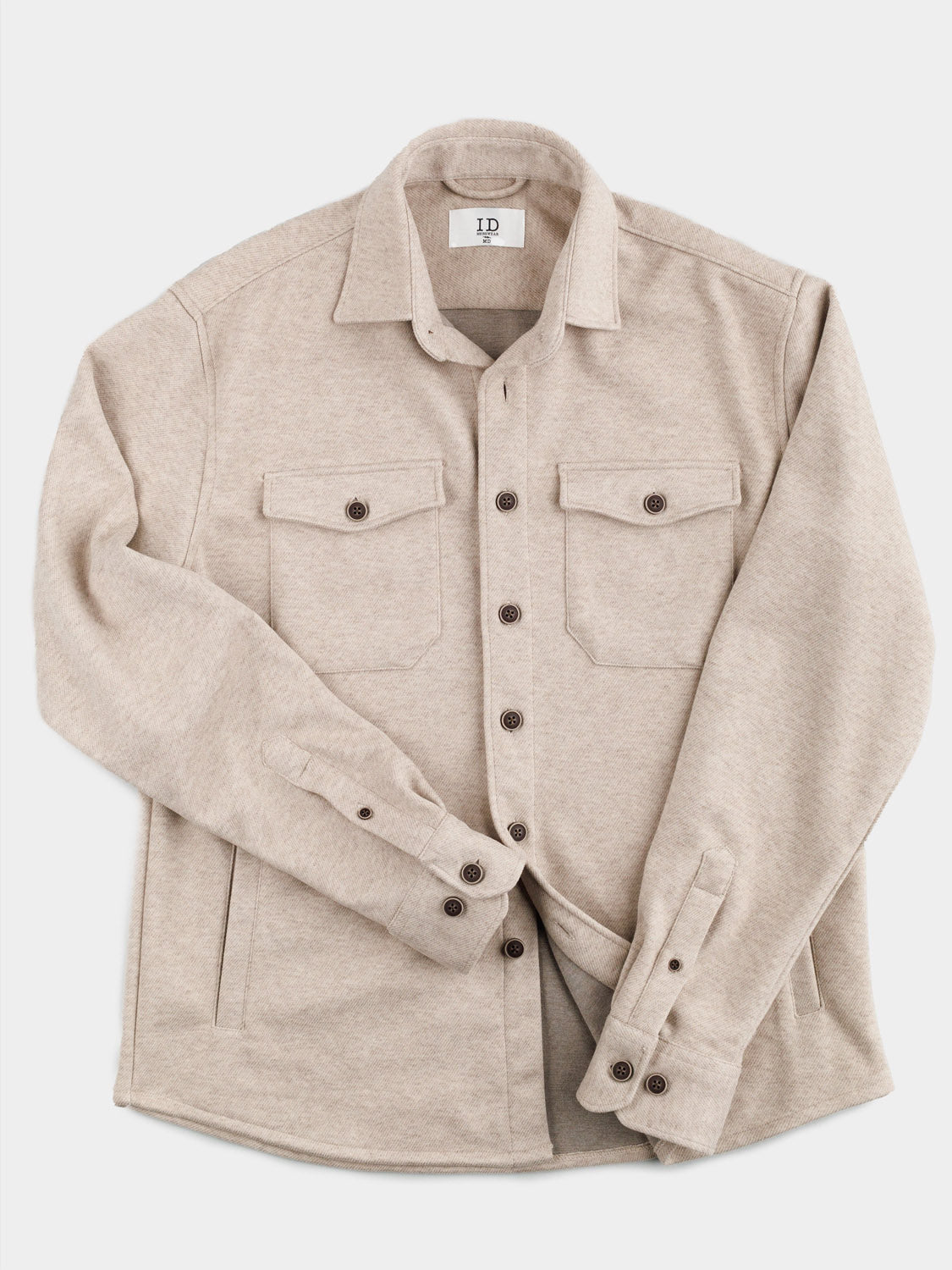 The ID Menswear Yukon Shirt Jacket, a beige button-up with a soft texture, is showcased against a white background. Ideal for casual outings and transitional weather, it has two chest pockets with buttoned flaps and dark buttons on the front and cuffs.