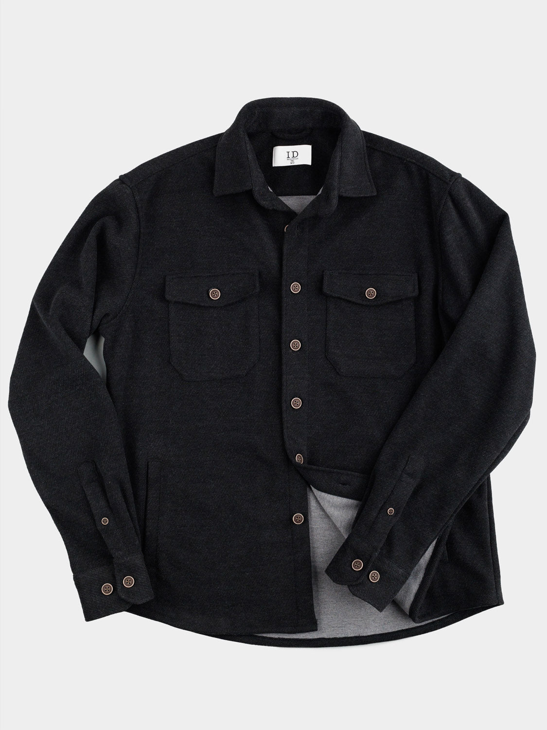 ID Menswears Yukon Shirt Jacket, featuring two flap chest pockets and contrasting brown buttons, is ideal for casual outings and transitional weather. Stylishly presented against a plain white background, this black wool button-up exudes effortless charm.