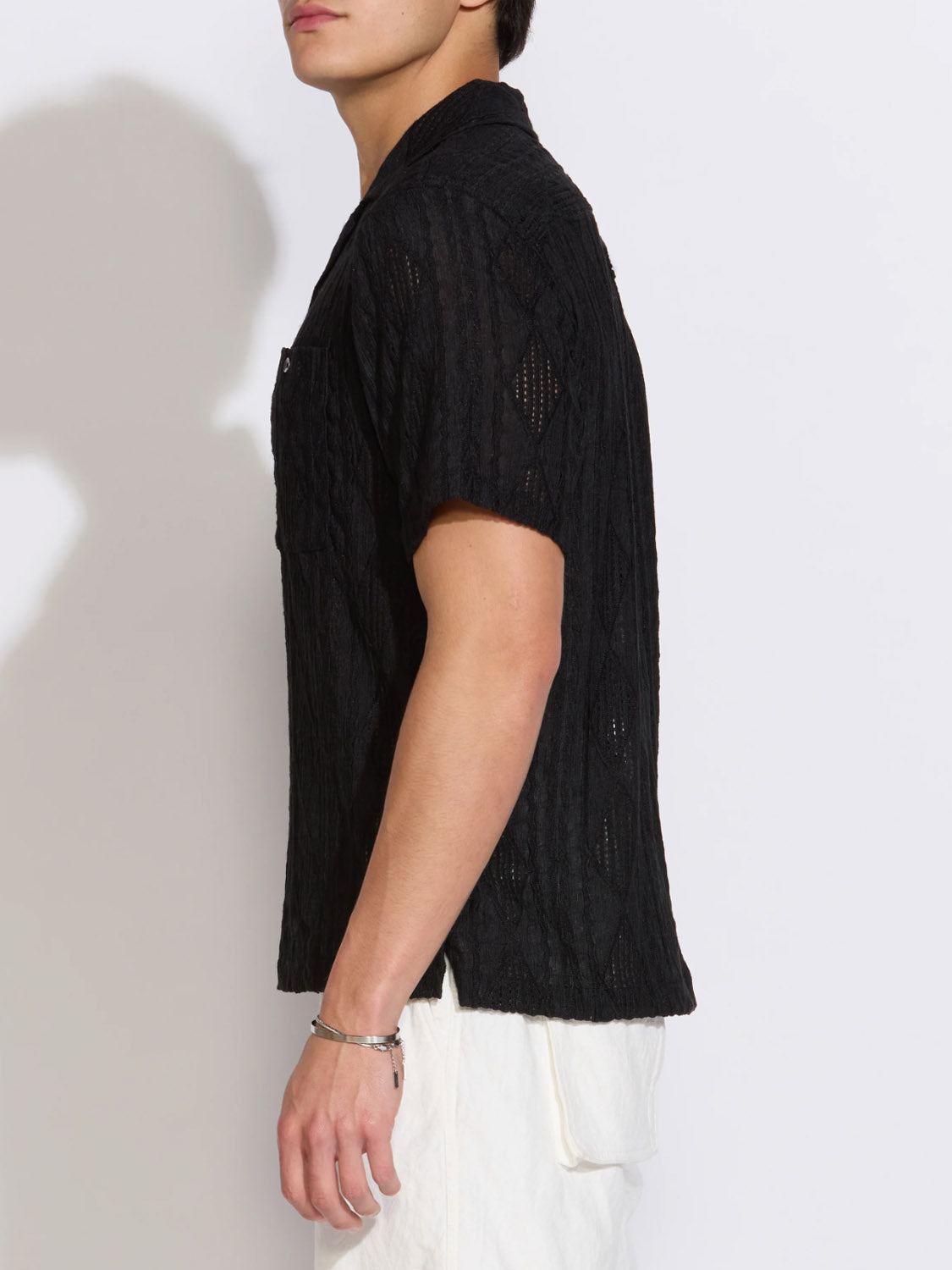 A person wearing the Civil Society Zacatecas Jacquard Knit Resort Shirt in black and white pants stands sideways against a plain light background, with only their upper body and part of their face visible.