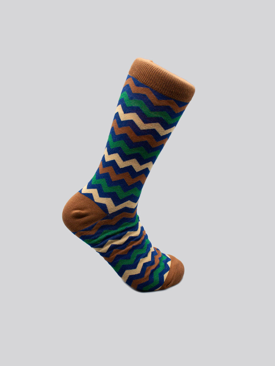 The Zigster Graphic Socks by ID Menswear feature a colorful zigzag pattern in blue, green, cream, and brown on light gray combed cotton, with brown toe, heel, and cuff for a stylish touch.
