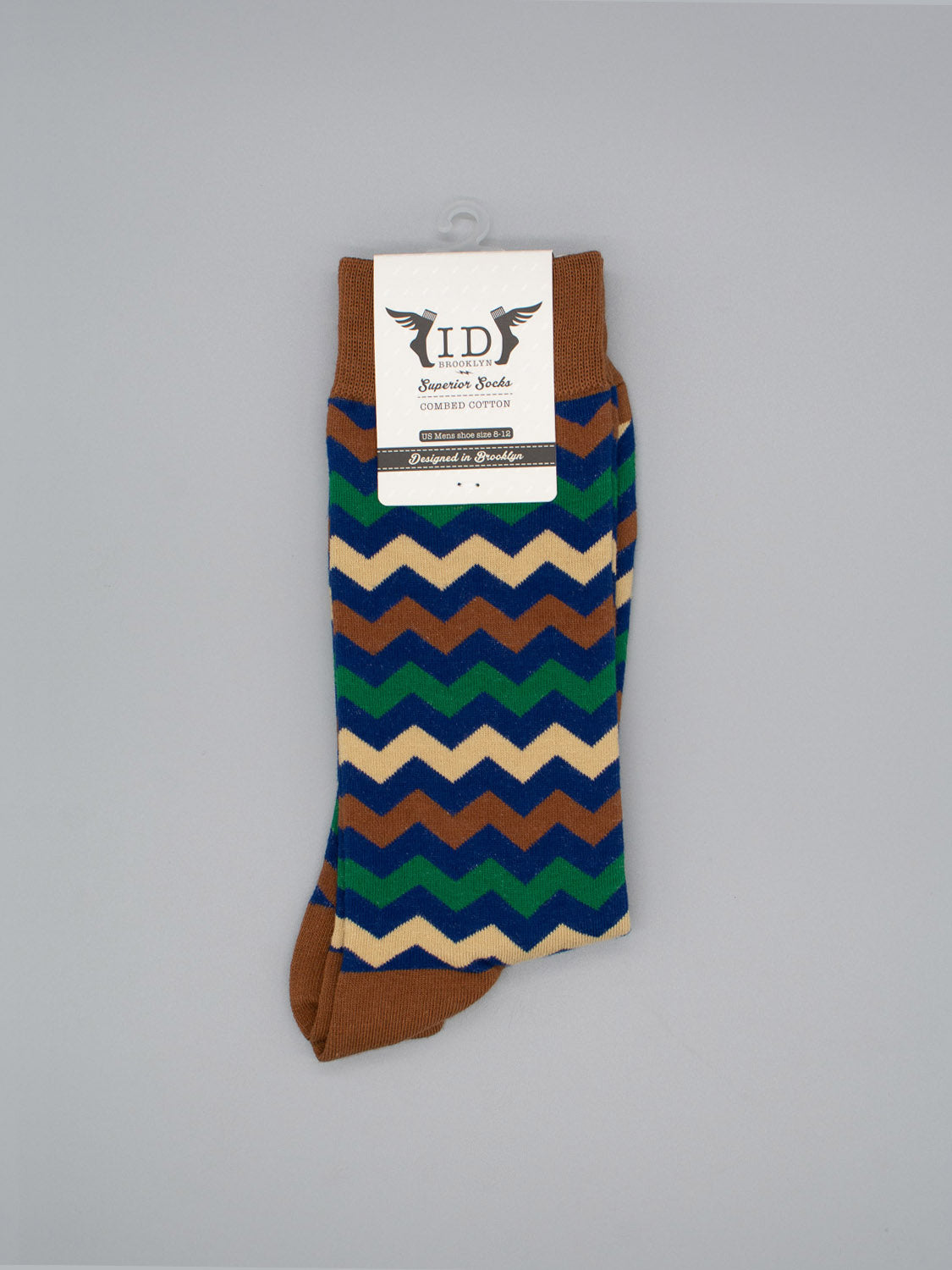 Zigster Graphic Socks by ID Menswear feature brown, blue, green, and beige zigzag stripes in high-quality combed cotton, packaged with an ID Designer Socks label on a light gray background.