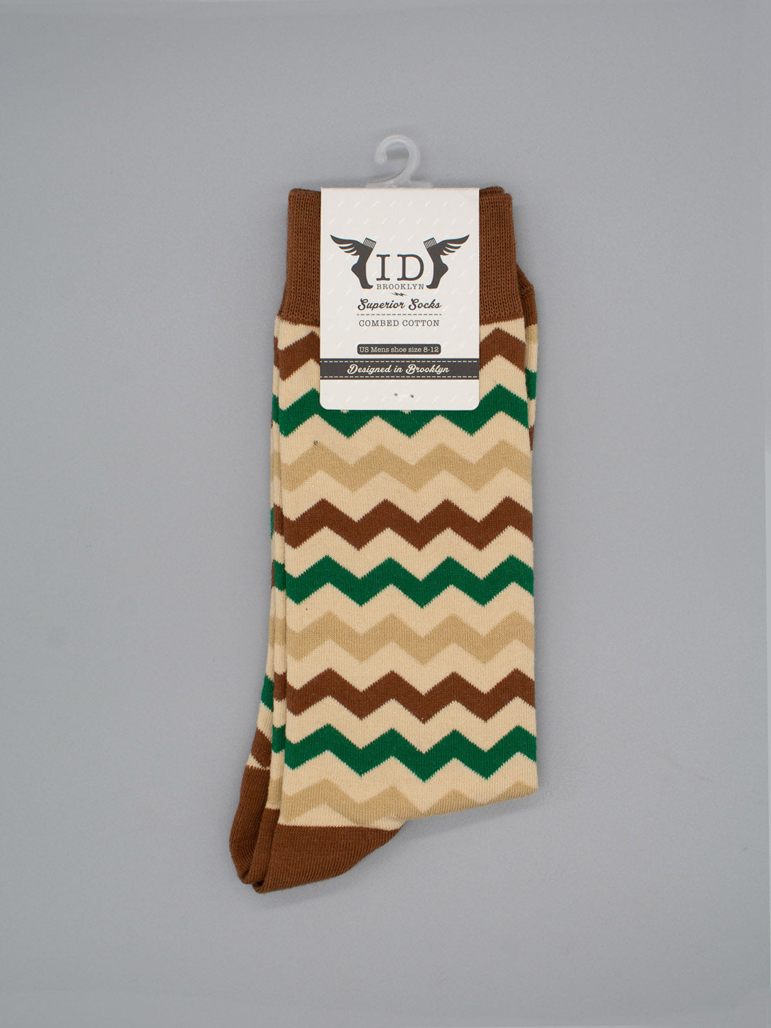 The Zigster Graphic Socks by ID Menswear feature a brown, beige, green, and cream zigzag pattern, made from high-quality combed cotton and shown against a gray background with a white top label.