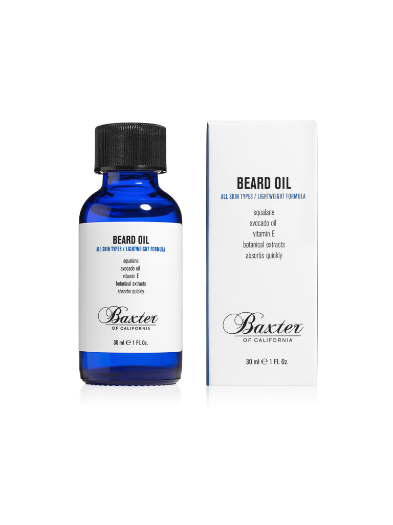 A blue glass bottle of Baxter Beard Oil with a black cap sits next to its white box. The label highlights grooming ingredients such as squalane, avocado oil, vitamin E, and botanical extracts.