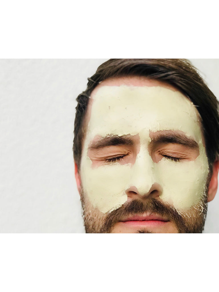 A man with his eyes closed wears Baxter's Clay Mask AHA, a thick light green detoxifying facial mask, against a plain white background.