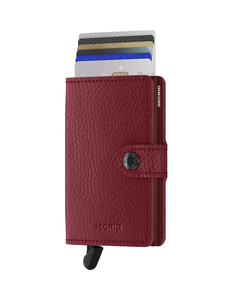 The Secrid Miniwallet Vegetable Tanned Leather is a red leather wallet with a snap button, RFID protection, and a black lever at the bottom for easy card access. It holds several cards, which are partially visible at the top.