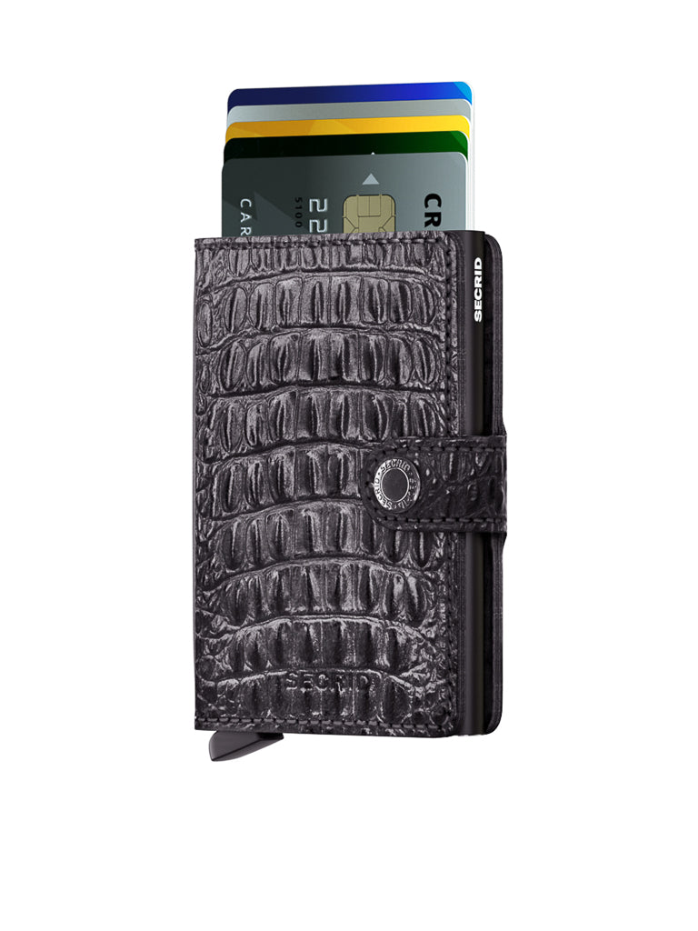 The Secrid Miniwallet Nile, featuring a black crocodile pattern in premium European leather, stands upright against a white background with its snap closure securing partially visible credit cards at the top.