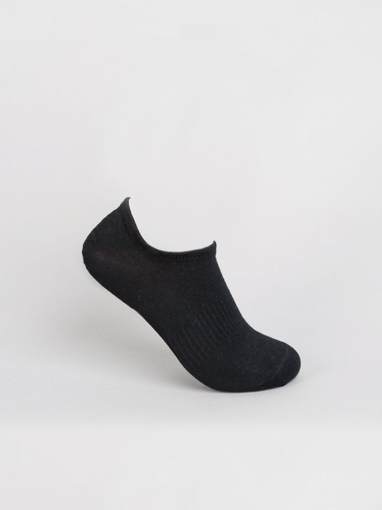 A single black No Show Ribbed Sock from ID Menswear is showcased on a white background. Made of combed cotton, it is slightly elevated to highlight its simple, unadorned design and ribbed upper texture.