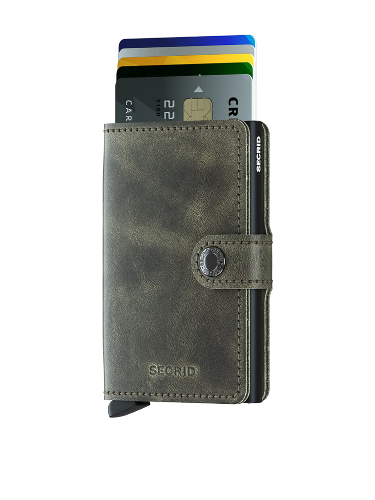 A Secrid Miniwallet Vintage Leather in green, featuring a snap closure and RFID protection, holds several partially ejected credit cards, displayed on a white background.