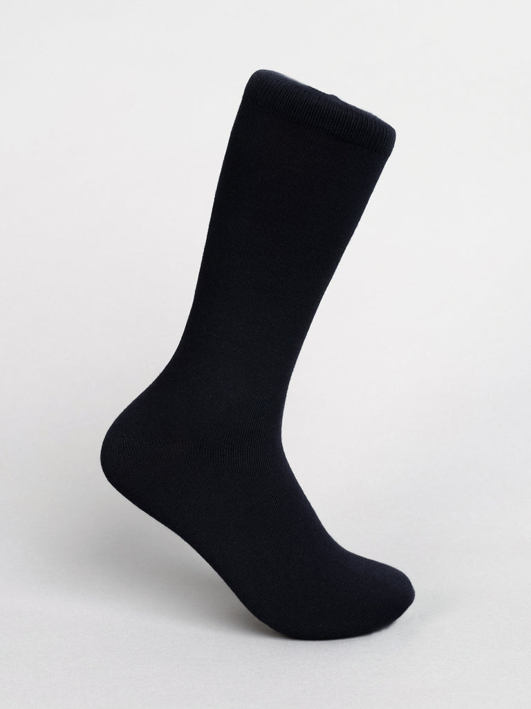 A black sock from ID Menswears Solid Color Combed Cotton Socks is displayed against a light gray background. The regular-sized, smooth-textured sock stands upright, appearing to rest on an invisible foot, ideal for everyday comfort.