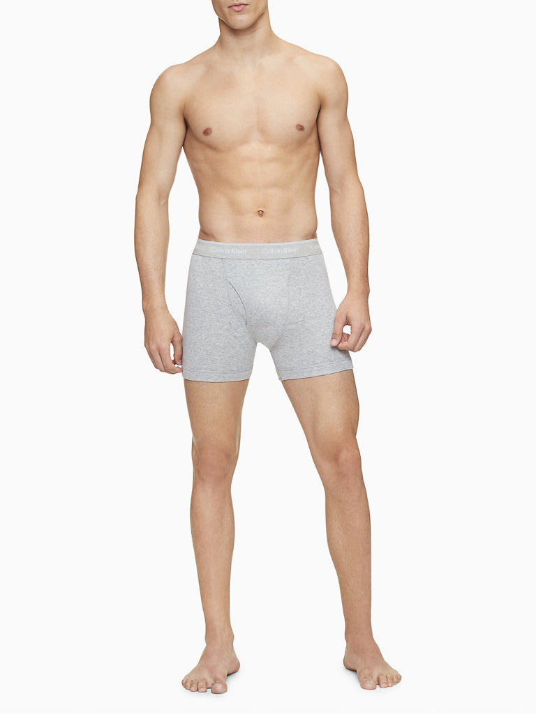 A shirtless man stands facing forward wearing Calvin Klein NB4003 3-Pack Cotton Classic Boxer Briefs, barefoot on a white background with his arms relaxed at his sides.