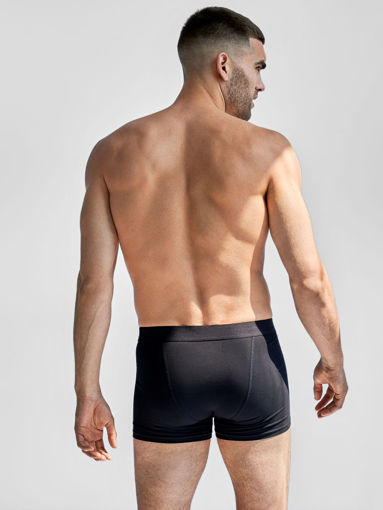 A man with short dark hair models Bread & Boxers 3 Pack Boxer Briefs, crafted from organic cotton. The black boxers feature an elastic waistband for comfort against a simple, light-colored background.