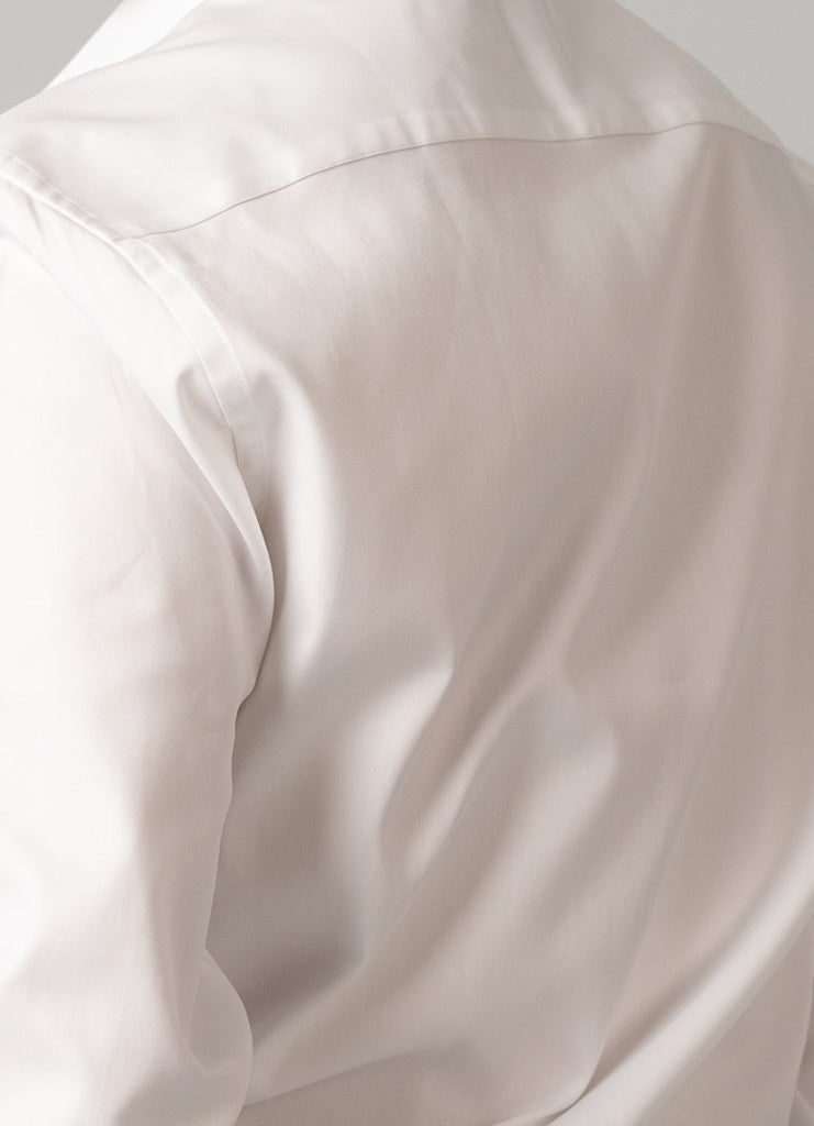Close-up of a person wearing an ID Menswears ID Cotton Dress Shirt, slim fit in white, with smooth fabric, slight creases, and shoulder seam visible against a plain background.