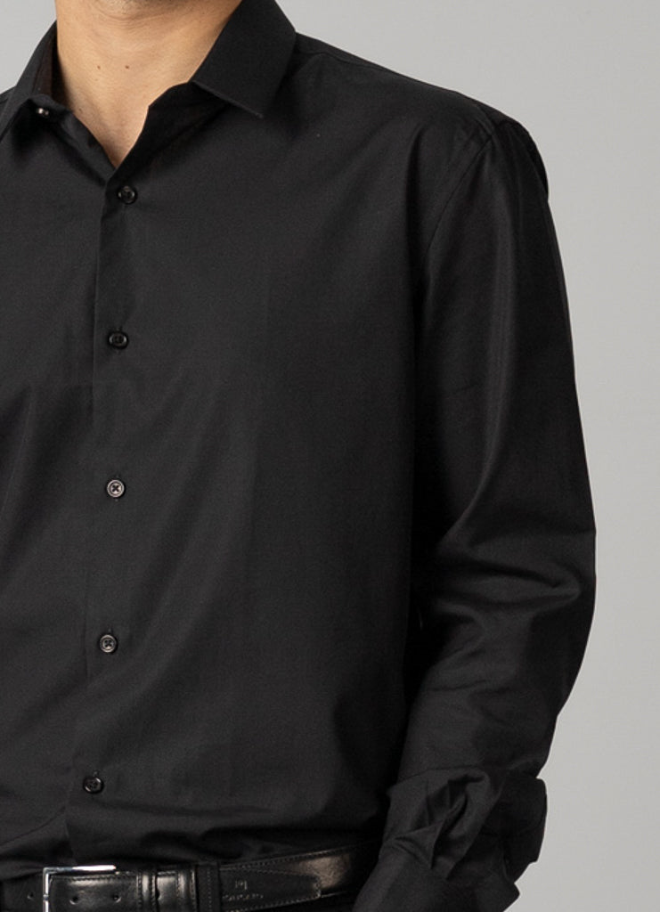 A model is shown from the chest down wearing an ID Menswear ID Cotton Dress Shirt in slim fit, buttoned and with rolled-up sleeves. Its paired with a black belt featuring a silver buckle against a plain gray background, highlighting their sleek style.