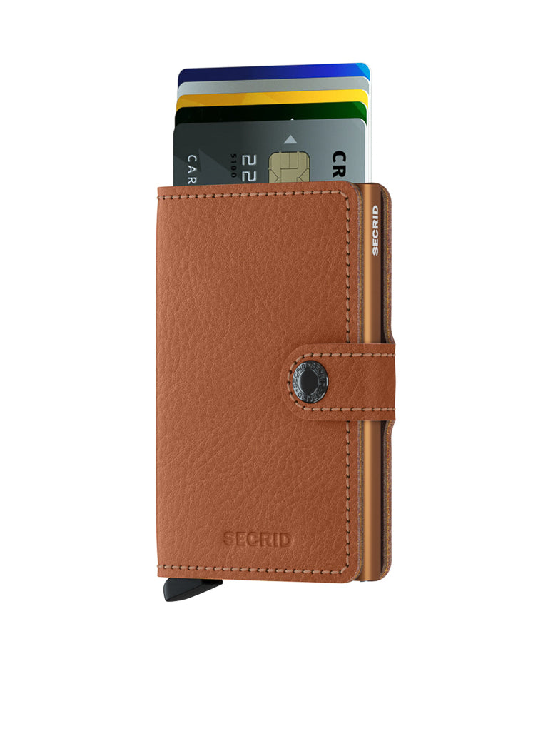 The Secrid Miniwallet Vegetable Tanned Leather in brown is shown upright with a snap closure and fanned credit cards partially visible. The wallet features RFID protection and stands against a white background.