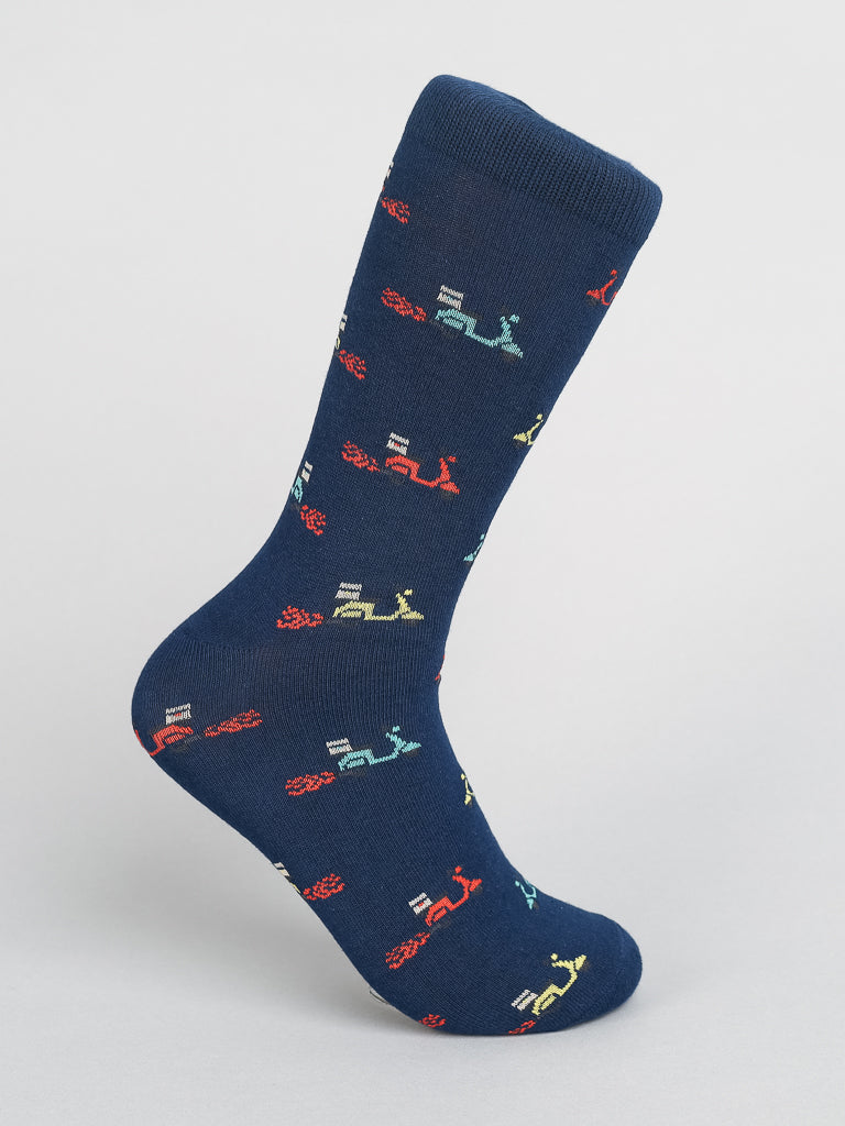 The Blazing Scooter Graphic Sock from ID Menswear features a whimsical design of colorful cartoon tractors in red, yellow, green, and blue on soft combed cotton for ultimate breathability, standing upright against a plain gray background.