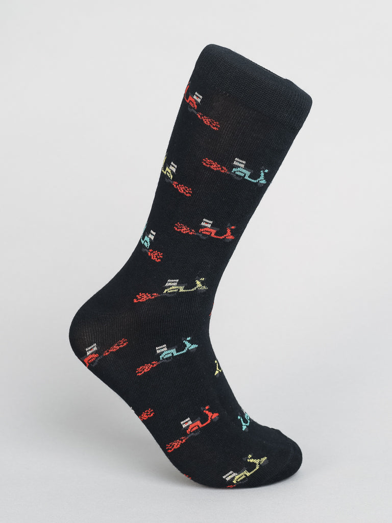 Introducing the ID Menswear Blazing Scooter Graphic Socks: made from combed cotton, these breathable socks feature a lively scooter pattern in red, green, yellow, and blue on sleek black fabric, beautifully highlighted against a plain white backdrop.