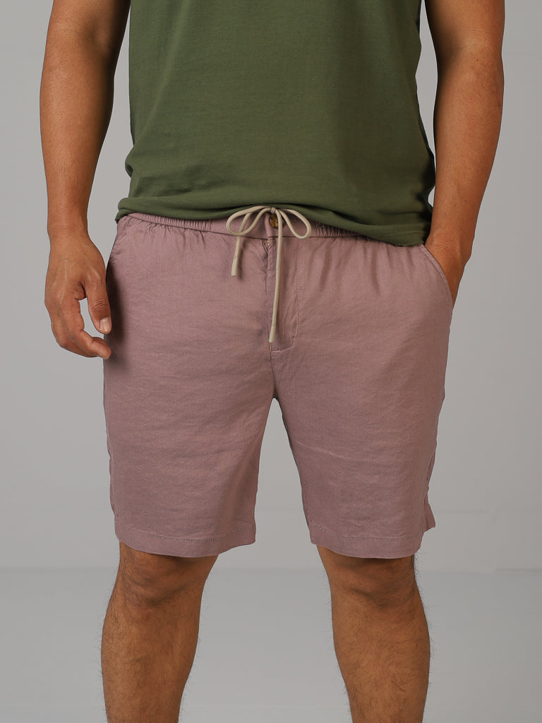 An individual poses against a plain backdrop, wearing a green shirt and cozy ID Menswears Driggs Linen Blend Short in mauve, ideal for warm weather.