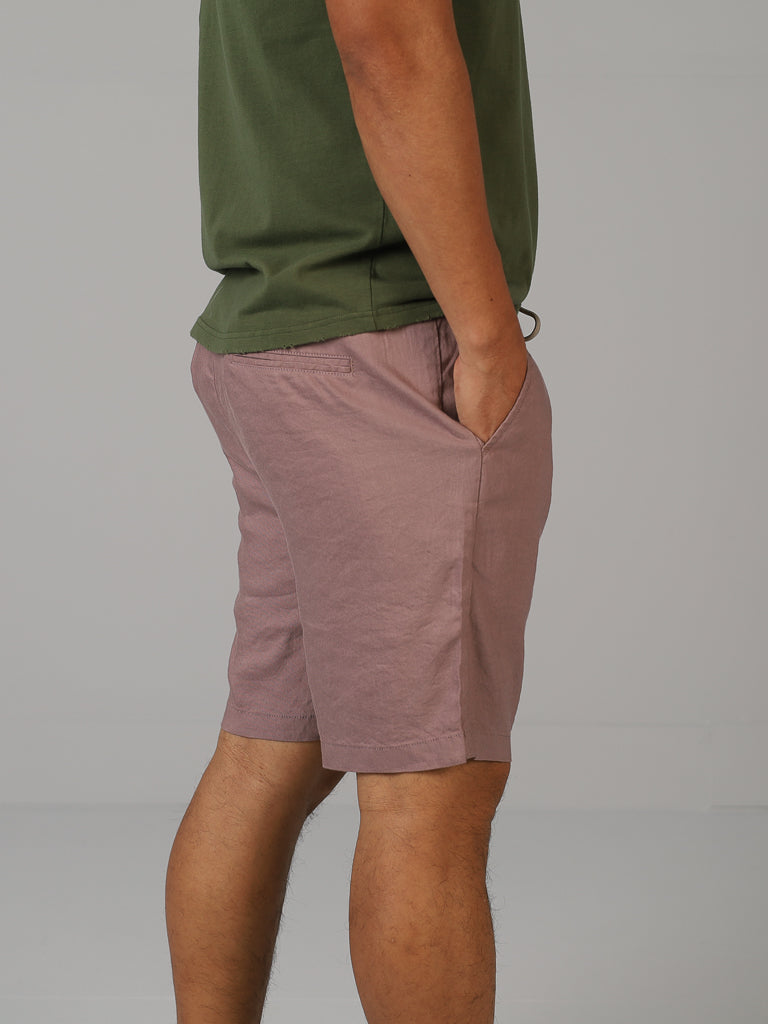 A person wearing a green t-shirt and ID Menswears Driggs Linen Blend Shorts stands with hands in pockets against a plain gray background.