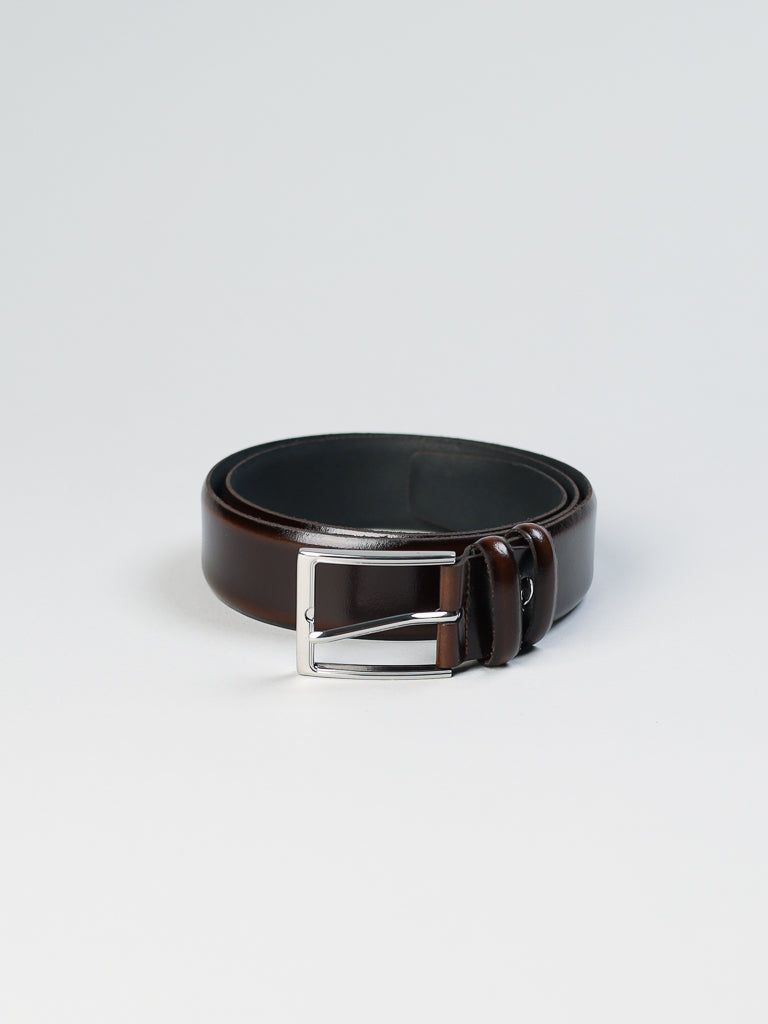 The ID Menswear 4903 Made in Italy Leather Belt, crafted from genuine coiled brown leather, showcases a shiny silver buckle and rests elegantly on a plain white surface in a minimalist style.