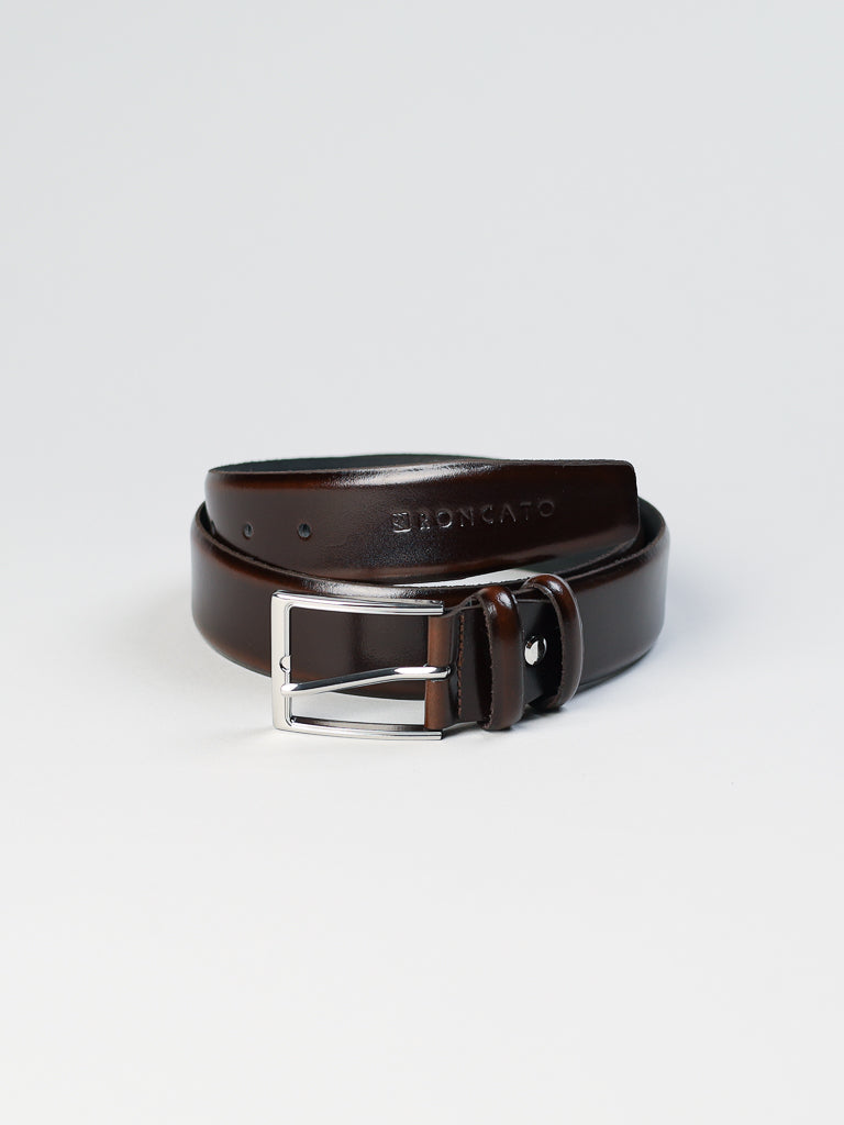 The 4903 Made in Italy Leather Belt by ID Menswear is crafted from dark brown genuine leather and features a silver buckle. Embossed with branding, it sits neatly coiled against a light gray backdrop, effortlessly blending craftsmanship and style.