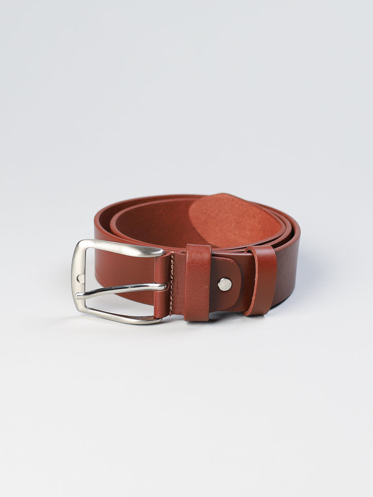 A coiled 4550 Made in Italy Leather Belt from ID Menswear, featuring brown genuine leather and a shiny silver buckle, rests on a light gray surface.