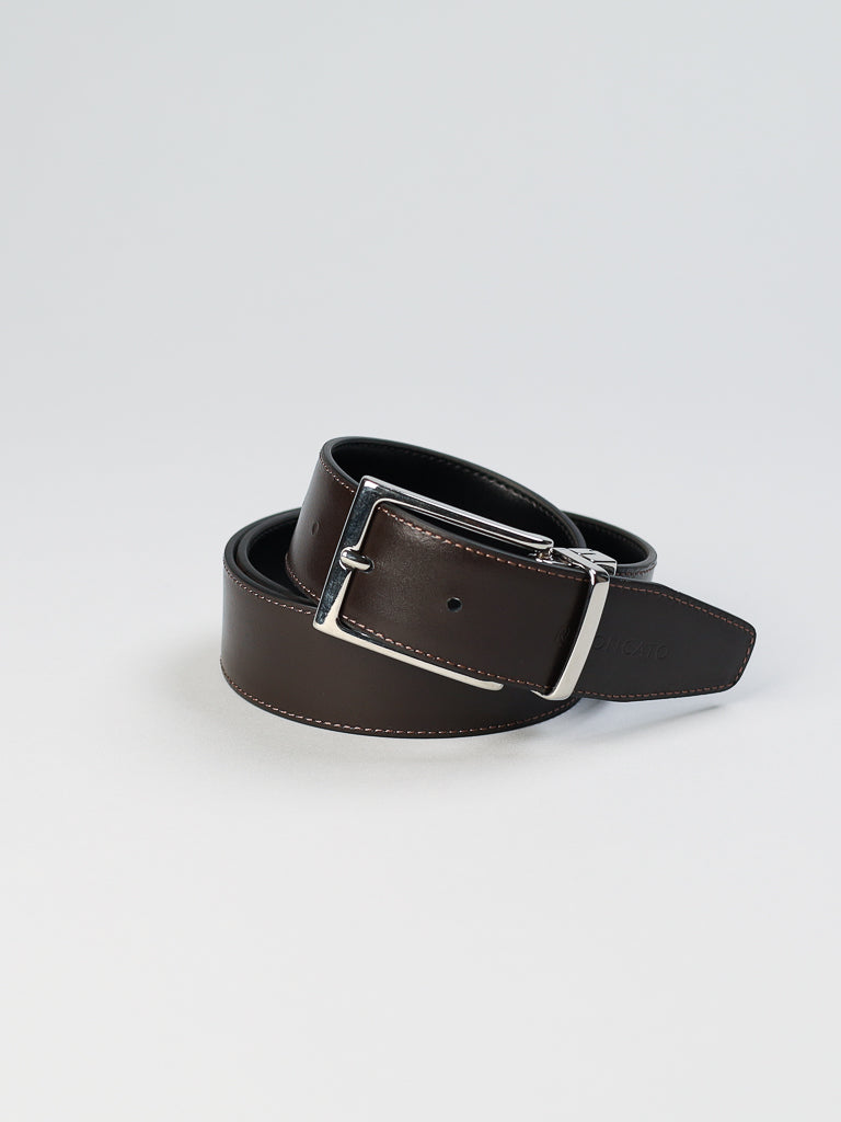 On a plain white surface lies the coiled ID Menswear 4026 Made in Italy Reversible Leather Belt, crafted from genuine dark brown leather. It features meticulous edge stitching and a silver buckle.