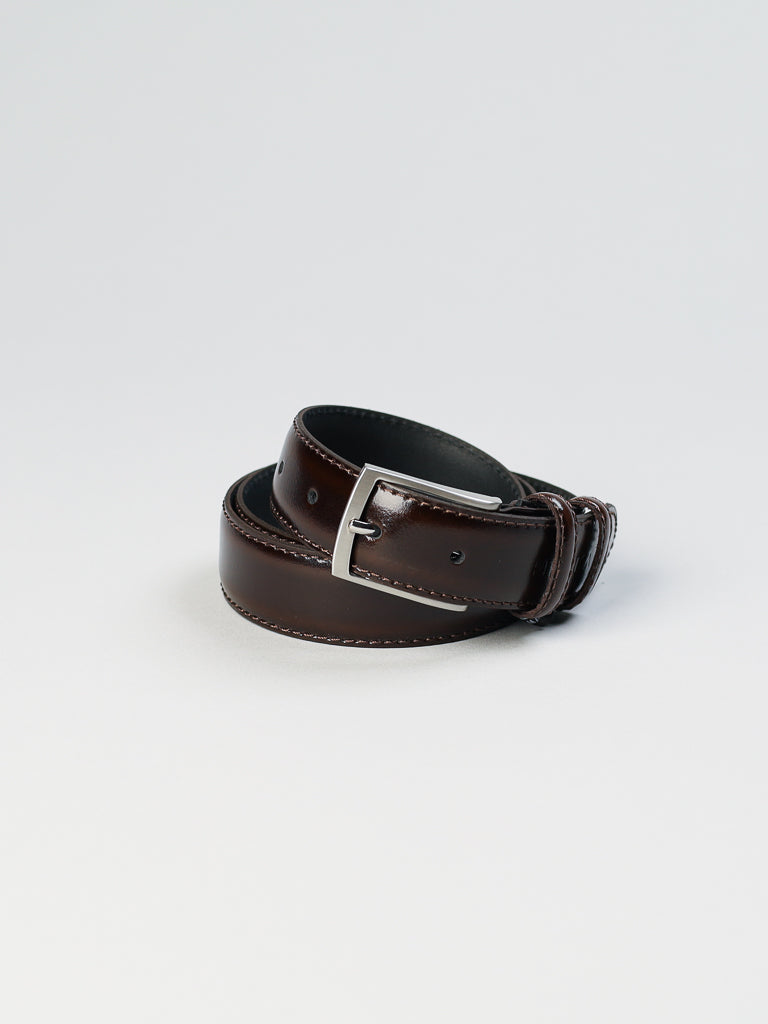 The 4904 Made in Italy Leather Belt by ID Menswear, featuring a coiled dark brown genuine leather strap and a solid metal buckle, is beautifully showcased against a plain light background.