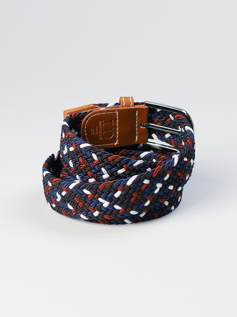 The ID Braided Stretch Woven Belt by ID Menswear is elegantly rolled up, displaying navy, red, white, and brown tones. It features a metal buckle and a brown leather end on a plain light gray background.