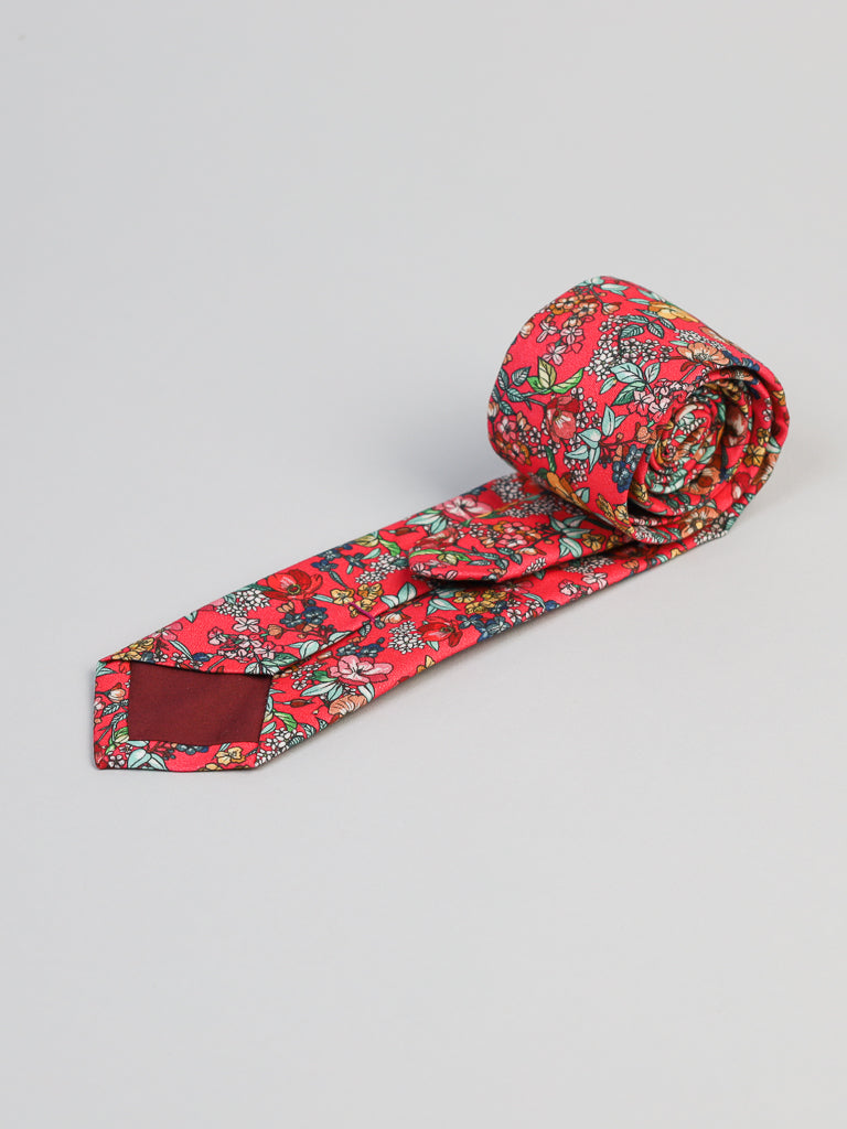 The P. Bouquet Cotton Tie by ID Menswear features a colorful red floral pattern with green, blue, and yellow accents. Handmade in Brooklyn, this tie is displayed on a light gray background—ideal for business formal occasions.