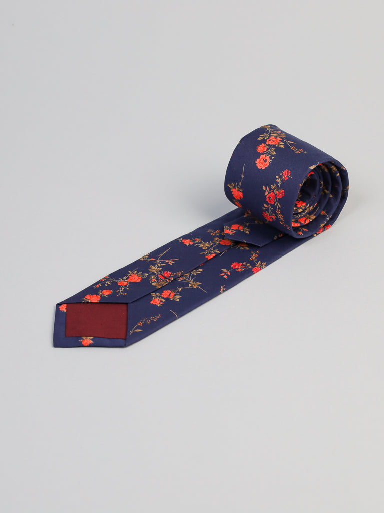 A neatly rolled Liberty of London Tana Lawn™ Elizabeth Tie by ID Menswear, featuring a red and orange floral pattern on navy blue, handmade in Brooklyn and displayed on a light gray background.