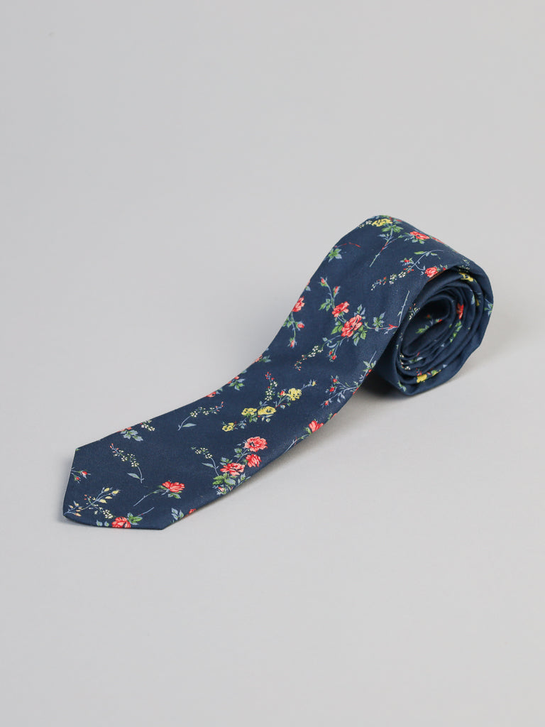 The Liberty of London Tana Lawn™ Elizabeth Tie by ID Menswear features a navy blue base with a colorful floral pattern of small red, yellow, and green flowers, crafted from soft cotton and neatly rolled on a light gray background.