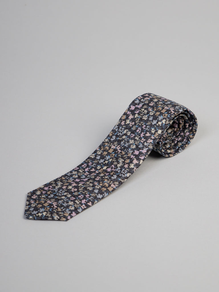 The Liberty of London Tana Lawn™ Gizmo Tie by ID Menswear features a small multicolored floral print on a dark background, made from luxurious cotton and shown rolled up on a light gray surface.