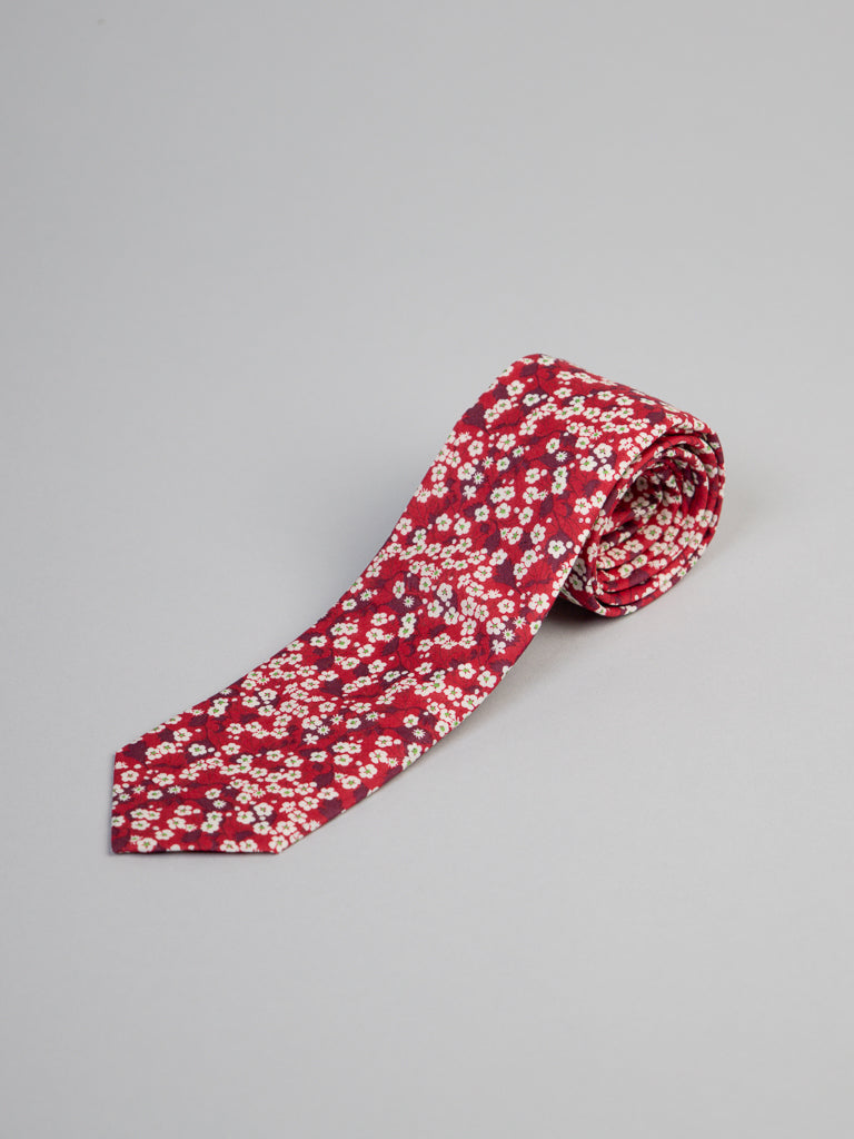 The Liberty of London Tana Lawn™ Valeria Tie by ID Menswear features a red base with white and light pink floral patterns, handmade in Brooklyn from luxurious cotton, neatly rolled and shown on a plain light gray background.