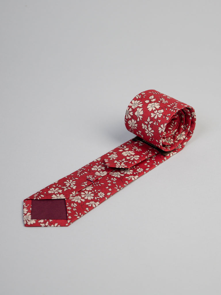 The Liberty of London Tana Lawn™ Carpel Tie by ID Menswear is handmade in Brooklyn from premium Tana Lawn cotton, featuring a red base with small white flowers and displayed neatly rolled on a plain light gray background.